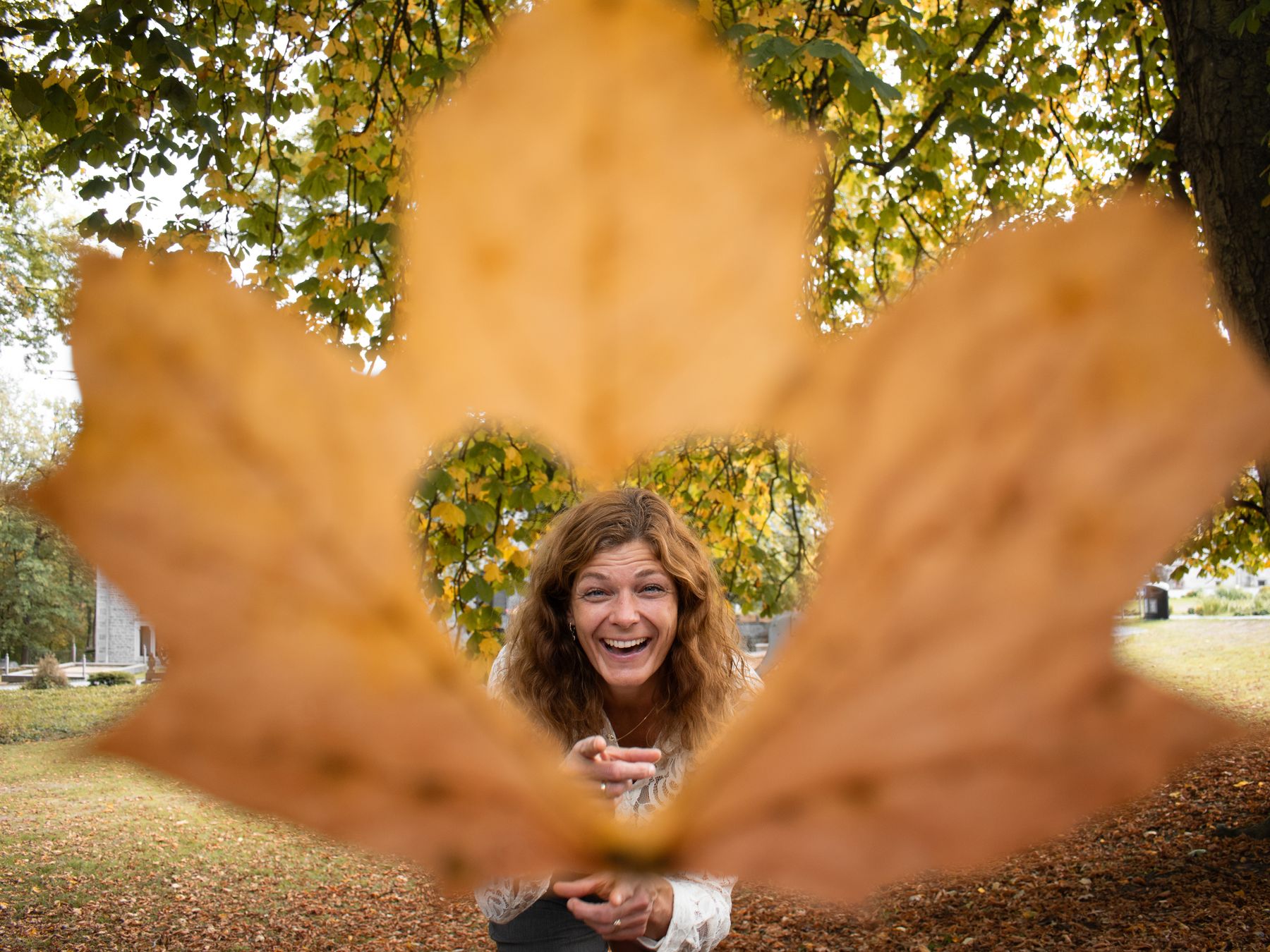 Jantine kijkt lachend door een uitgesneden hart in een herfstblad