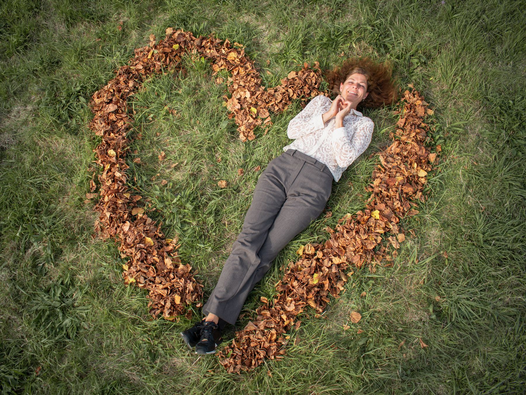 Jantine ligt lachend in een hart van herfstbladeren